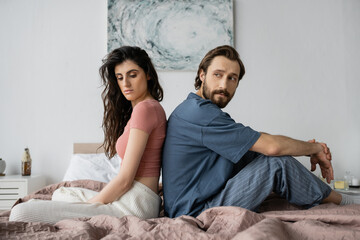 Wall Mural - Upset woman in pajama sitting back to back with asexual boyfriend on bed.