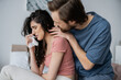 © LIGHTFIELD STUDIOS - Caring man in pajama hugging crying girlfriend with napkin in bedroom.
