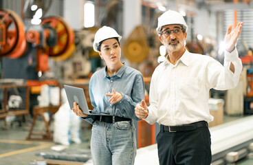 Two professional engineer,worker,technician use clipboard discuss work, walk in steel metal manufacture factory plant industry. Black African American man and woman wear hard hat check quality machine