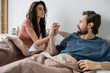 Brunette woman touching hand of asexual boyfriend on bed in morning.