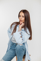 Wall Mural - Beautiful young stylish girl with a smile with long hair in fashionable casual clothes with a shirt and jeans sits on a white background