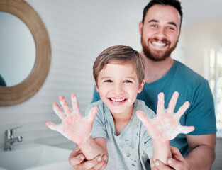 Poster - Germ free hands are happy hands. Portrait of a boy holding up his soapy hands while standing in a bathroom with his father at home.