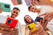 © Xavier Lorenzo - Low angle view of young group of millennial people in circle using smart mobile phones together outdoors. Joyful student friends looking at smartphone screen enjoying social media content