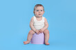 Little child sitting on baby potty against light blue background
