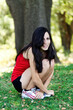 Hispanic Woman Squatting Outdoors Red Top Black Shorts