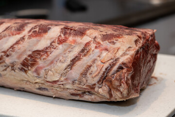 Wall Mural - A large rack of raw beef prime rib on a white industrial plastic cutting board. The meat is sitting on the kitchen counter next to a large bulb of garlic. The roast has rows of fat on each rib.