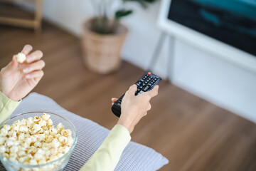 Wall Mural - Asian woman Watching smart TV and using remote controller Hand holding television audio remote control at home with the remote control television