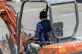 Fototapeta Panele - A man drives a digger on the street