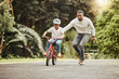 © S Fanti/peopleimages.com - You can do it. Shot of an adorable boy learning to ride a bicycle with his father outdoors.