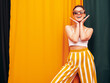 © halayalex - Fashion young beautiful smiling female in trendy summer white top t-shirt and yellow striped pants clothes. Sexy carefree woman posing near colourful textile background in studio. Positive model