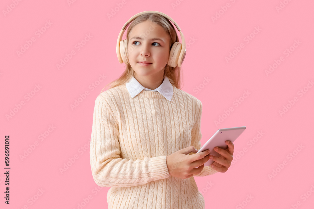 Little girl in headphones using tablet computer on pink background