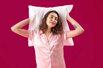 Poster - Young brunette woman in pajamas with pillow on pink background