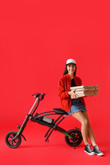 Canvas Print - Young woman with boxes of tasty pizza and electric bike on red background