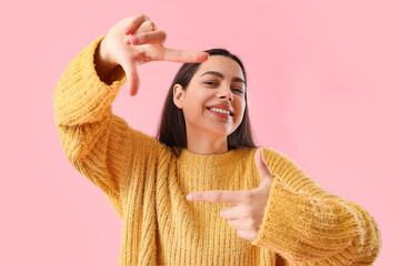 Beautiful young woman making frame with her fingers on pink background