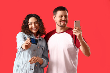 Wall Mural - Young couple with credit card and mobile phone on red background