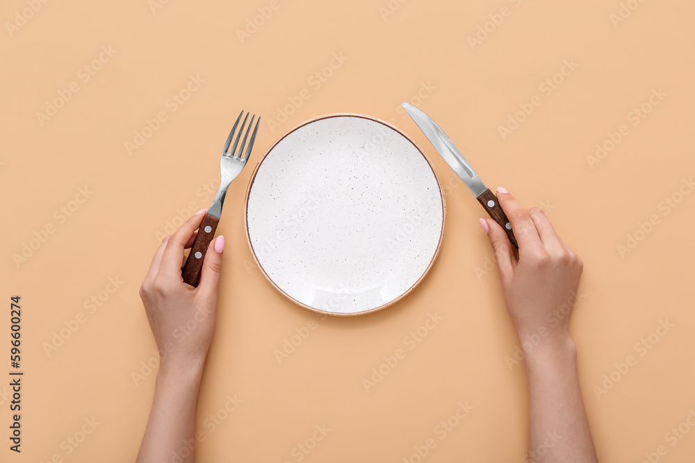 Woman with cutlery and empty plate on beige background