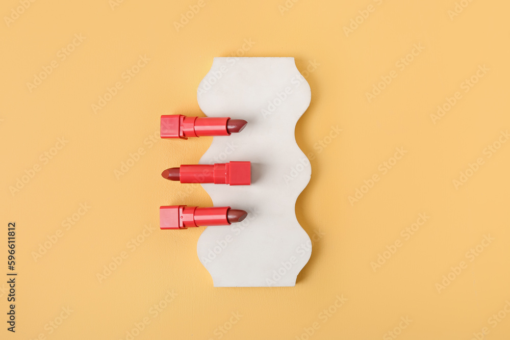 Decorative plaster podium with set of lipsticks on yellow background
