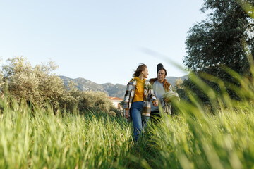 Young middle age couple walking along happily talking in park. Mature couple in summer park. Man and woman in casual clothes with guitar and picnic bag outside in spring nature.