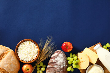 Jewish holiday Shavuot concept. Flat lay cottage cheese, bottle of milk, cereal bread, grape, apples, wheat on blue background.