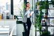 © nenetus - Beautiful elegant business woman talking with smartphone while holding some notes standing next to the window in a modern office