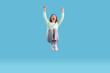 © Studio Romantic - Full body length shot of happy funny cheerful crazy excited young Caucasian woman in mint sweatshirt, grey trousers and white sneakers screaming and jumping high in the air on blue studio background