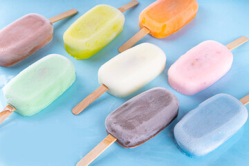 Wall Mural - Selection of multicolored ice cream popsicles. Various flavor gelato, frozen lollypops - chocolate vanilla blueberry strawberry pistachio orange, on light blue background