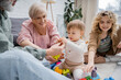 © LIGHTFIELD STUDIOS - smiling grandparents giving toys to toddler girl while playing together in living room.