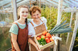 © Iryna - Organic farm food harvest concept. Portrait of laughing grandmother and her teen granddaughter in casual wear an apron holding wooden box full of fresh vegetables.