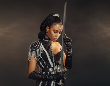 Portrait Fantasy African American Woman Warrior Holding Sword Weapon In Hand. Dark Queen Girl In Black Military Dress Costume. Gothic Lady Elf Fairy. Sexy Beauty Face Fashion Model Pray. Studio Photo