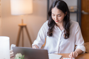 Wall Mural - Attractive happy young Asian businesswomen at home, sitting at the desk, using a laptop computer, tablet and headphones having a video chat.