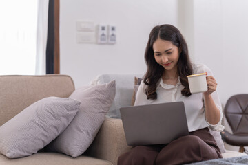 Wall Mural - Attractive happy young Asian businesswomen at home, sitting at the desk, using a laptop computer, tablet and headphones having a video chat.