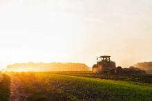 A Tractor In A Field Plows The Ground At Dawn, Sowing Grain. High Quality Photo