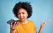 © Nicholas Felix/peopleimages.com - This text makes no sense. Shot of a young woman standing against a blue background in the studio and looking confused while using her cellphone.