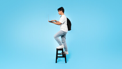 Wall Mural - Asian Student Guy Using Laptop Walking Up Stairs, Blue Background