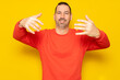 © Andres - Smiling bearded hispanic man 40s wearing casual pullover posing stretching hands for hug while noticing someone looking at camera isolated on yellow background studio portrait.