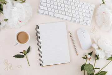 Feminine workspace with blank open notepad and cup of coffee milk, keyboard, stylish office writing supplies and on a pastel teble