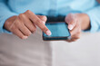 © Jesse B/peopleimages.com - Closeup of female hands holding and and scrolling on smartphone while standing inside a office at work. Business woman typing a message and using social media showing their screen