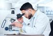 © C Coetzee/peopleimages.com - One serious young male medical scientist sitting at a desk and using a microscope to examine and analyse test samples on slides in a hospital. Hispanic healthcare biochemist professional discovering