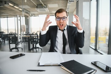 Wall Mural - Angry businessman sitting at the table and screaming.