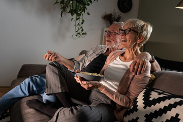 Wall Mural - Senior couple sitting on sofa and eating popcorn. They're joying watching the movie.	