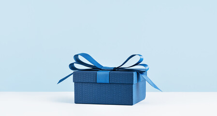 small Luxury gift box with a blue bow on light blue. Side view monochrome . Fathers day or Valentines day gift for him. Corporate gift concept or birthday party. Festive sale copy space