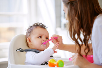 Sticker - Eat up little one. Shot an attractive young woman sitting in the kitchen with her daughter and feeding her.