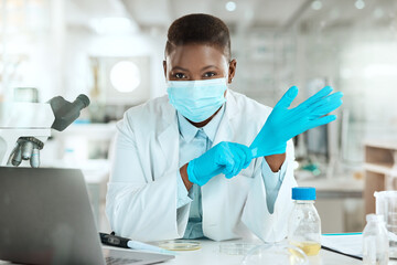 Wall Mural - Im ready to work with samples. Shot of a young scientist sitting alone in her laboratory and putting surgical gloves on.