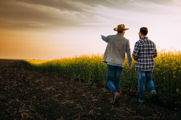 two farmers walking on a farmland at unset and talking.