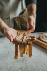 Wall Mural - Unrecognizable man in an apron holding dough cut into strips on a white table against a dark wall