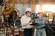 © Montri - two professional engineer,worker,technician use clipboard discuss work, walk in steel metal manufacture factory plant industry. Black African American man and woman wear hard hat check quality machine