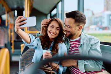 Cheerful couple taking selfie while riding in city bus.