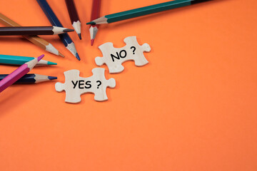 YES and NO are written on the missing puzzles on the orange background with colorful pencils at the side. Copy space for text and messages 