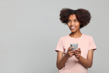 Wall Mural - Smiling African American woman with smartphone on light grey background. Space for text