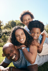 Wall Mural - Happy african american family of four lying stacked on top of each other while having fun and playing together in the sun. Carefree mother and two kids piled on top of father while bonding at the park